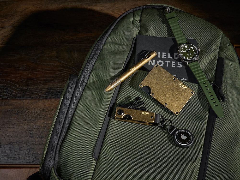 A Ridge brass wallet and key case on an olive Ridge backpack